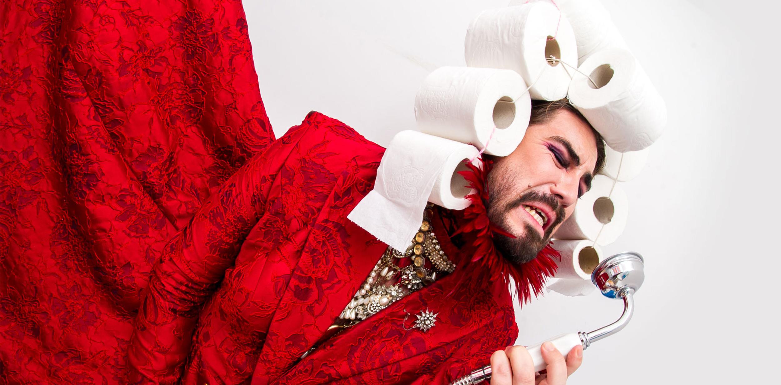 Drag queen singing into shower hose with a wig of loo rolls