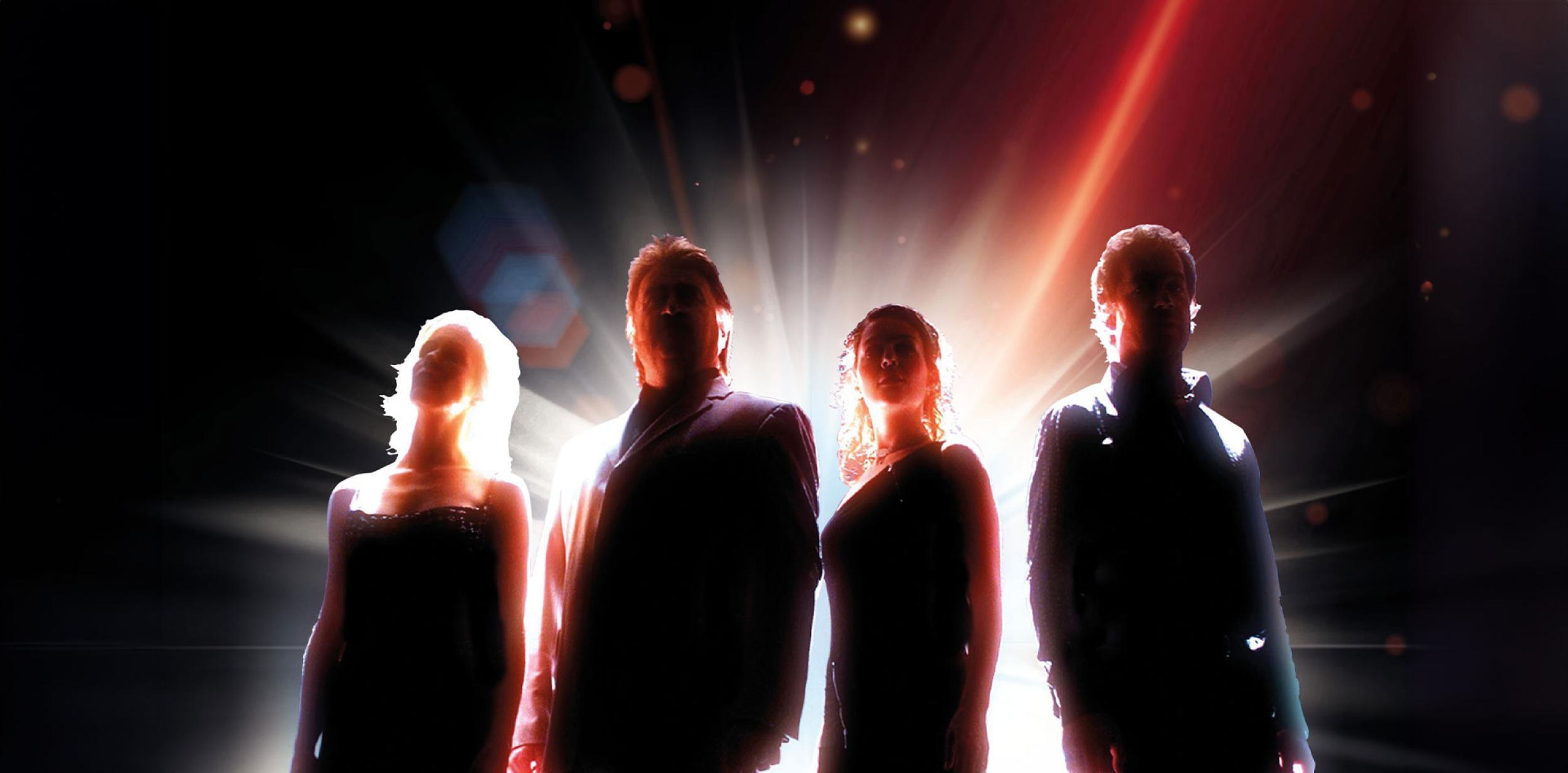 The silhouette of four people in front of a bright light