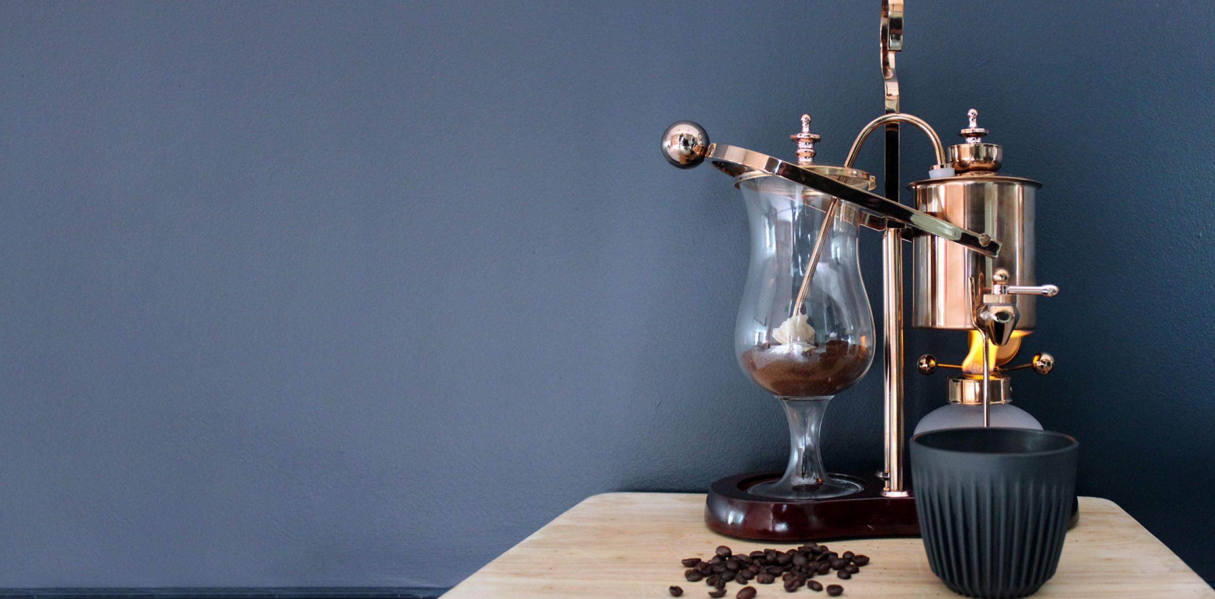 An old-style coffee machine sat upon a wooden table against a grey background