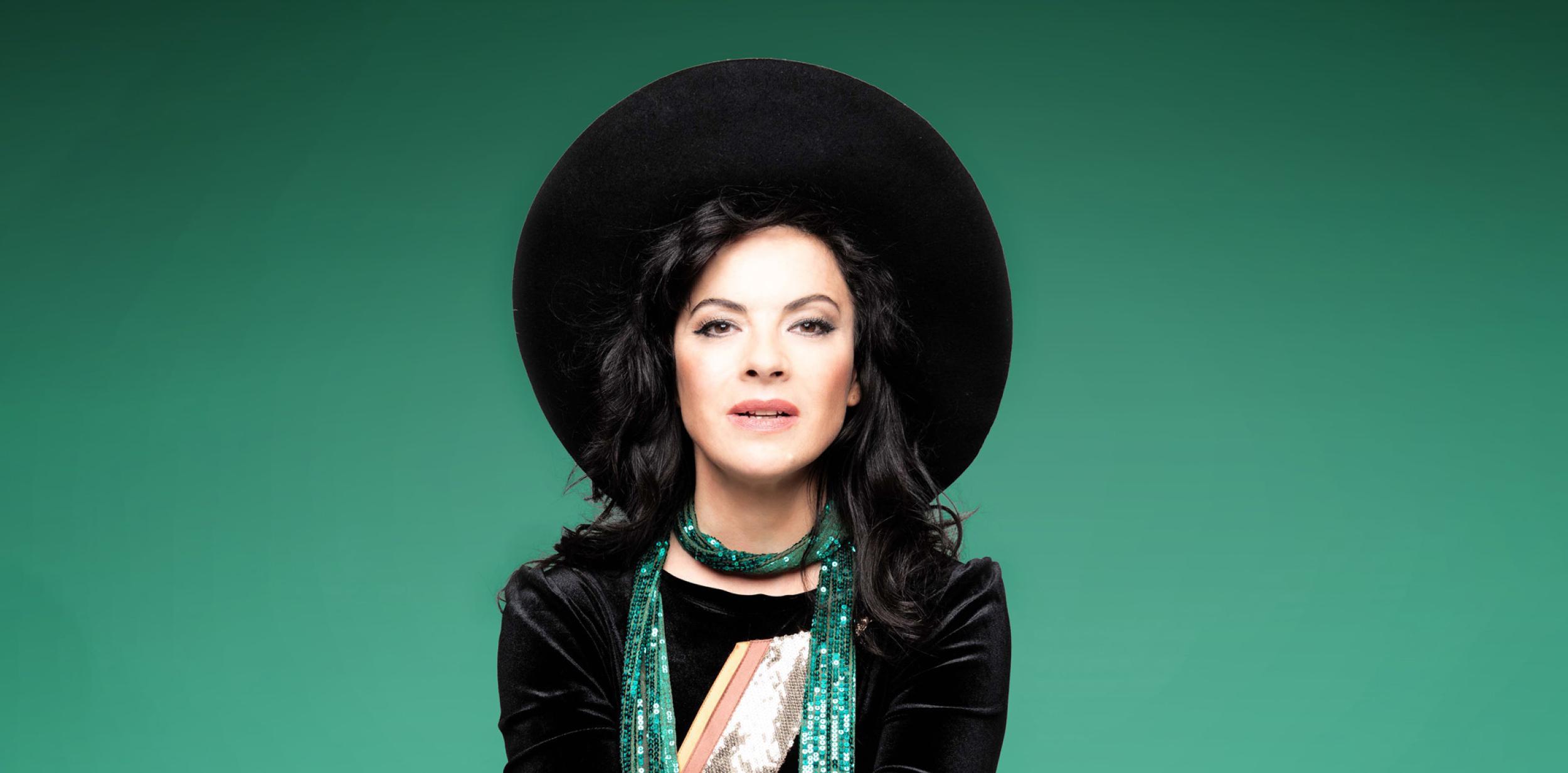 female in black hat jacket with green scarf against a green background