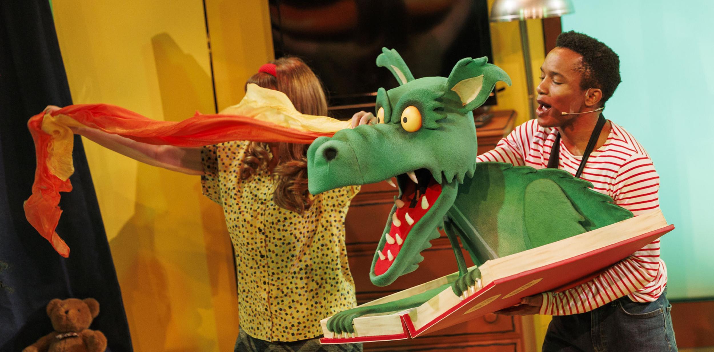 A large green dragon puppet emerging from an open book