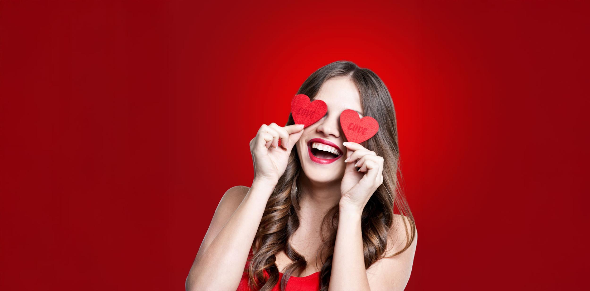 A person holding two paper love hearts over their eyes