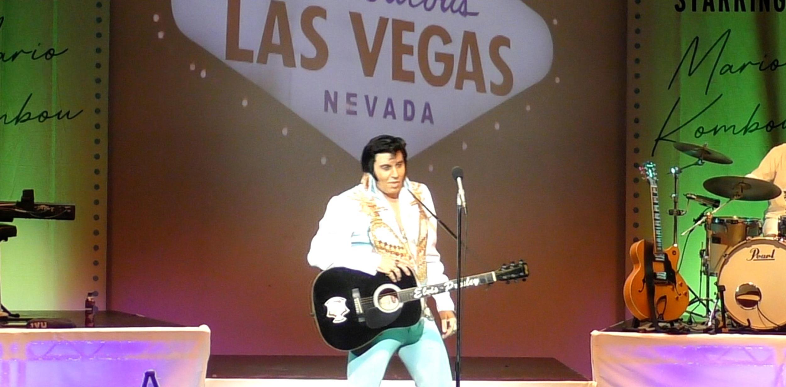 Elvis impersonator on stage with guitar in front of Las Vegas sign