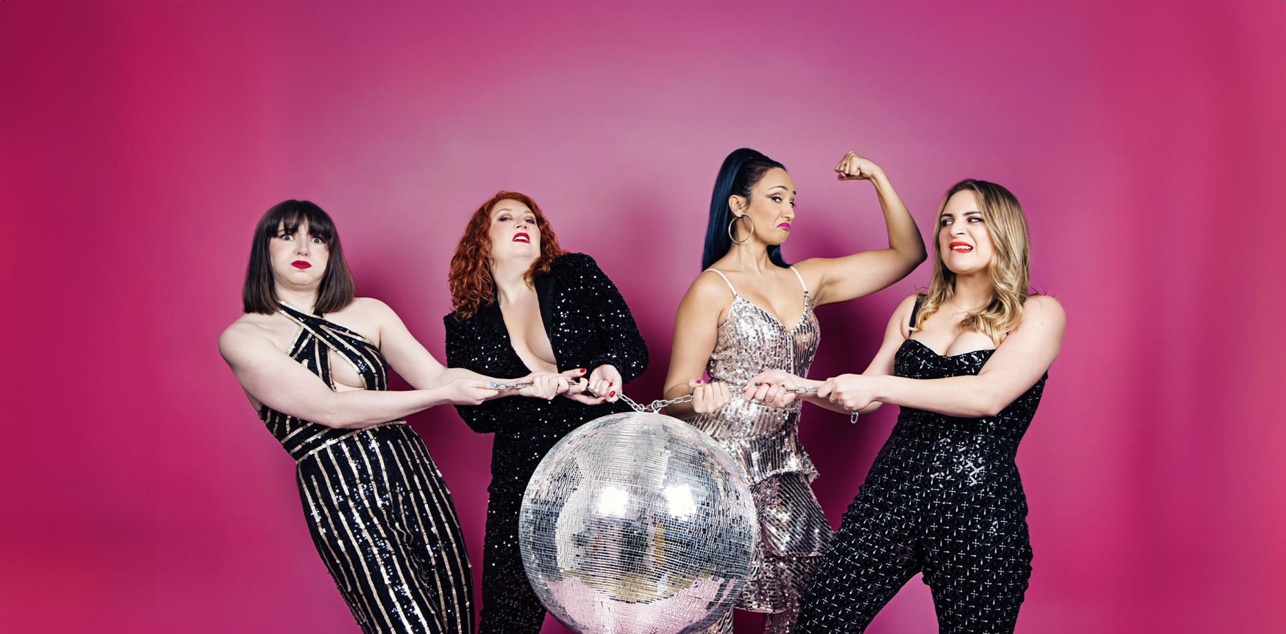 Four ladies wearing sparkly outfits and holding a disco ball