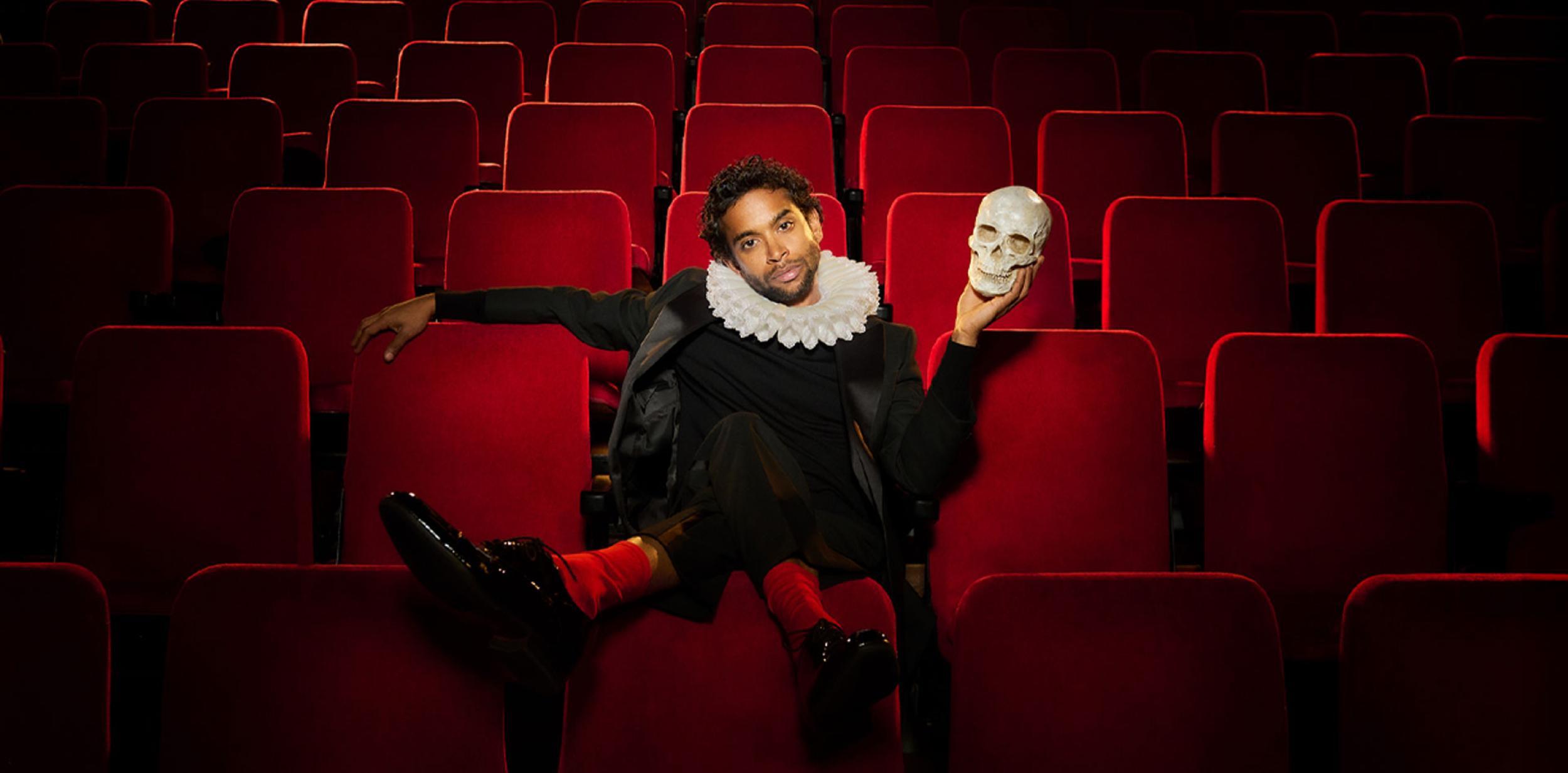 A person sitting in a theatre seat, holding a skull