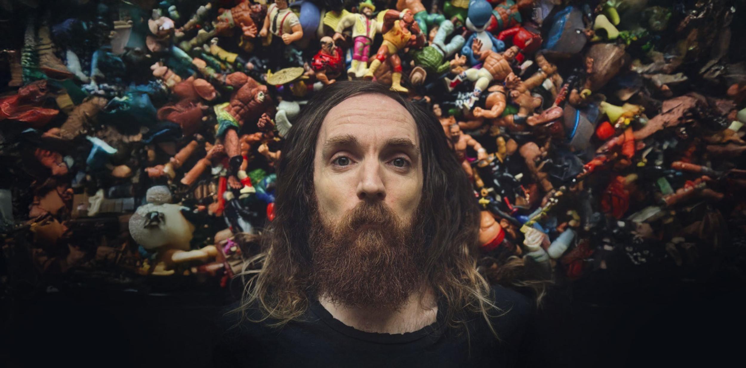 A person with a big beard and long hair, surrounded by small figurines