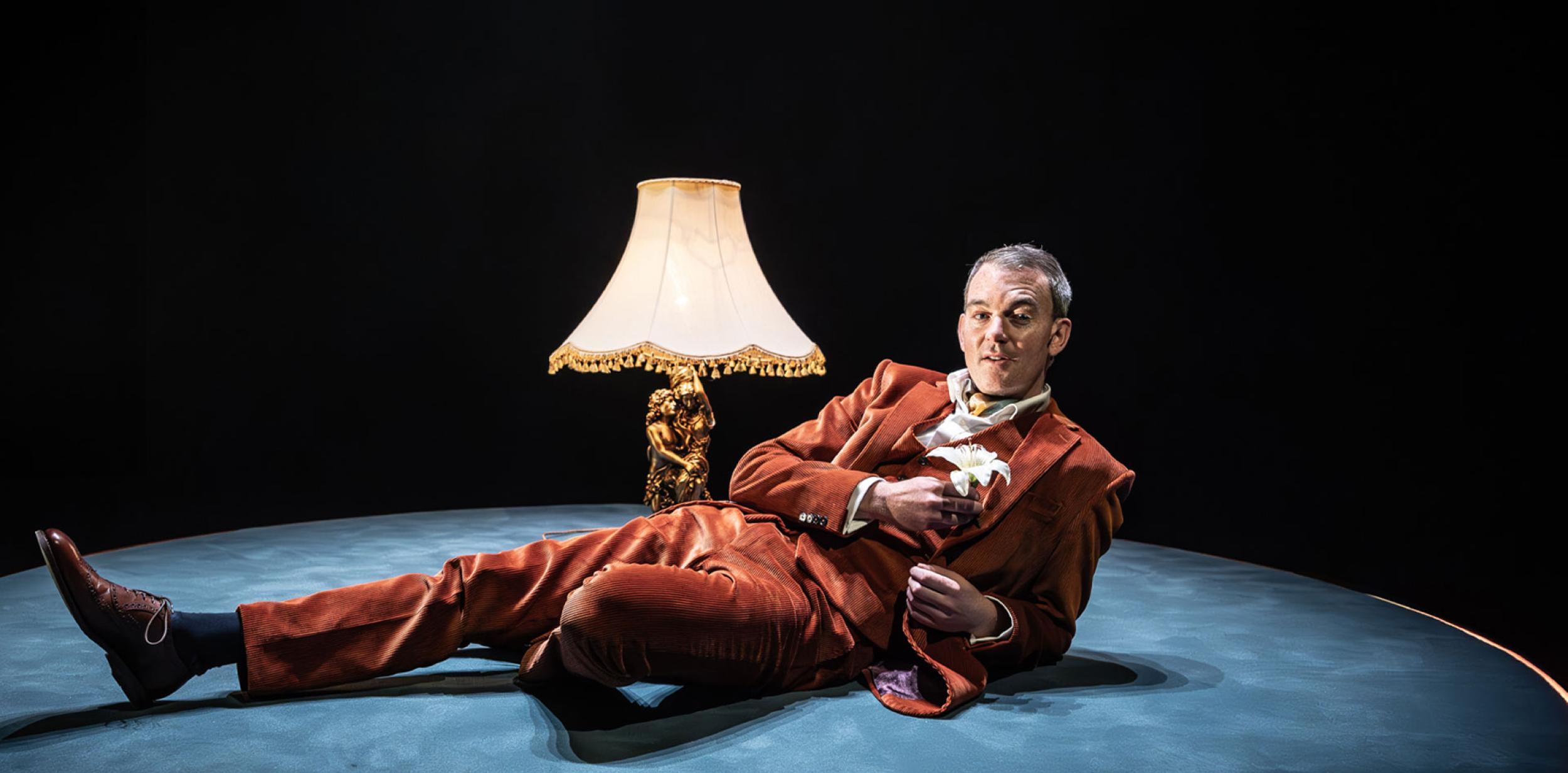 A person dressed in a suit laying on the floor next to a lamp