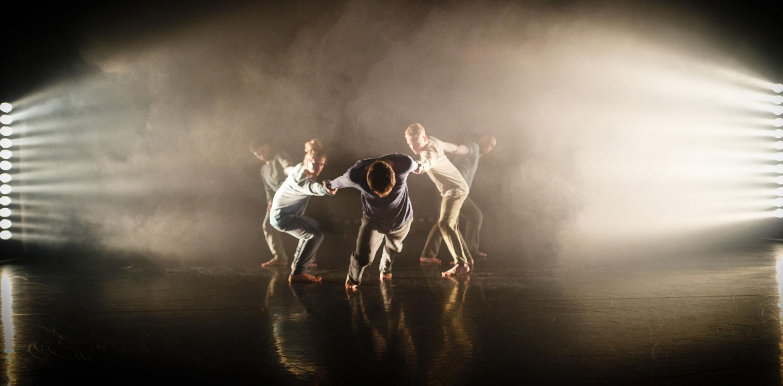 A group of male dancers performing on stage engulfed in haze and spotlights 