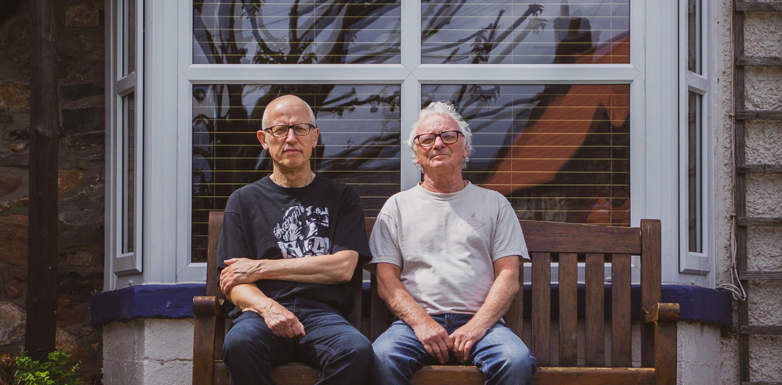 The Lindisfarne male duo sat on a bench in front of a bay window