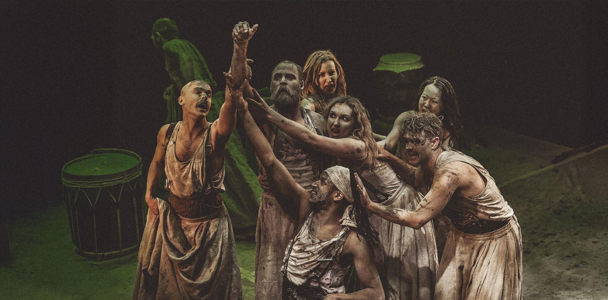 A group of people wearing robes, covered in clay and reaching up to the sky.