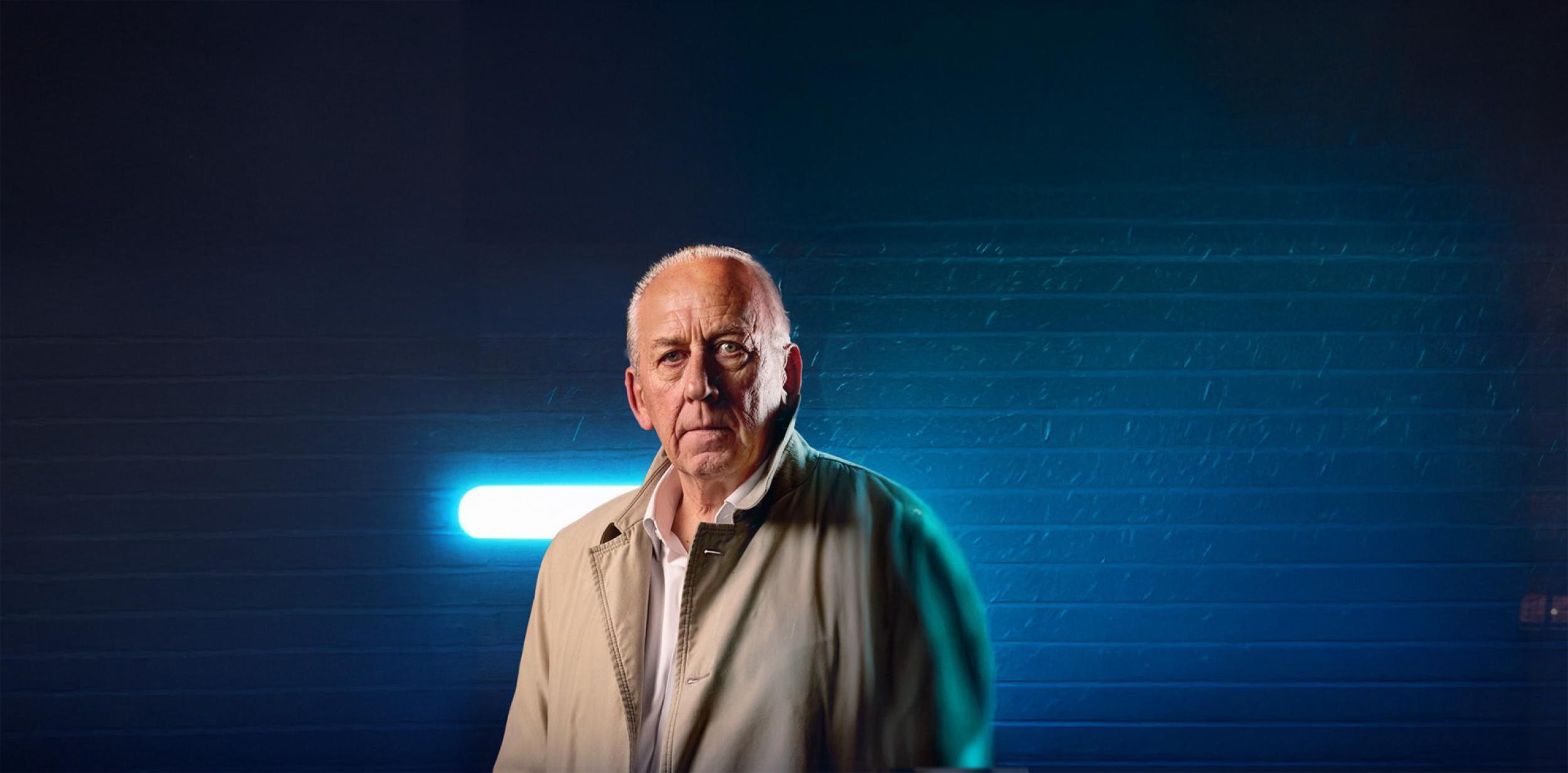 Peter Bleksley stood in front of brick wall lit up in blue