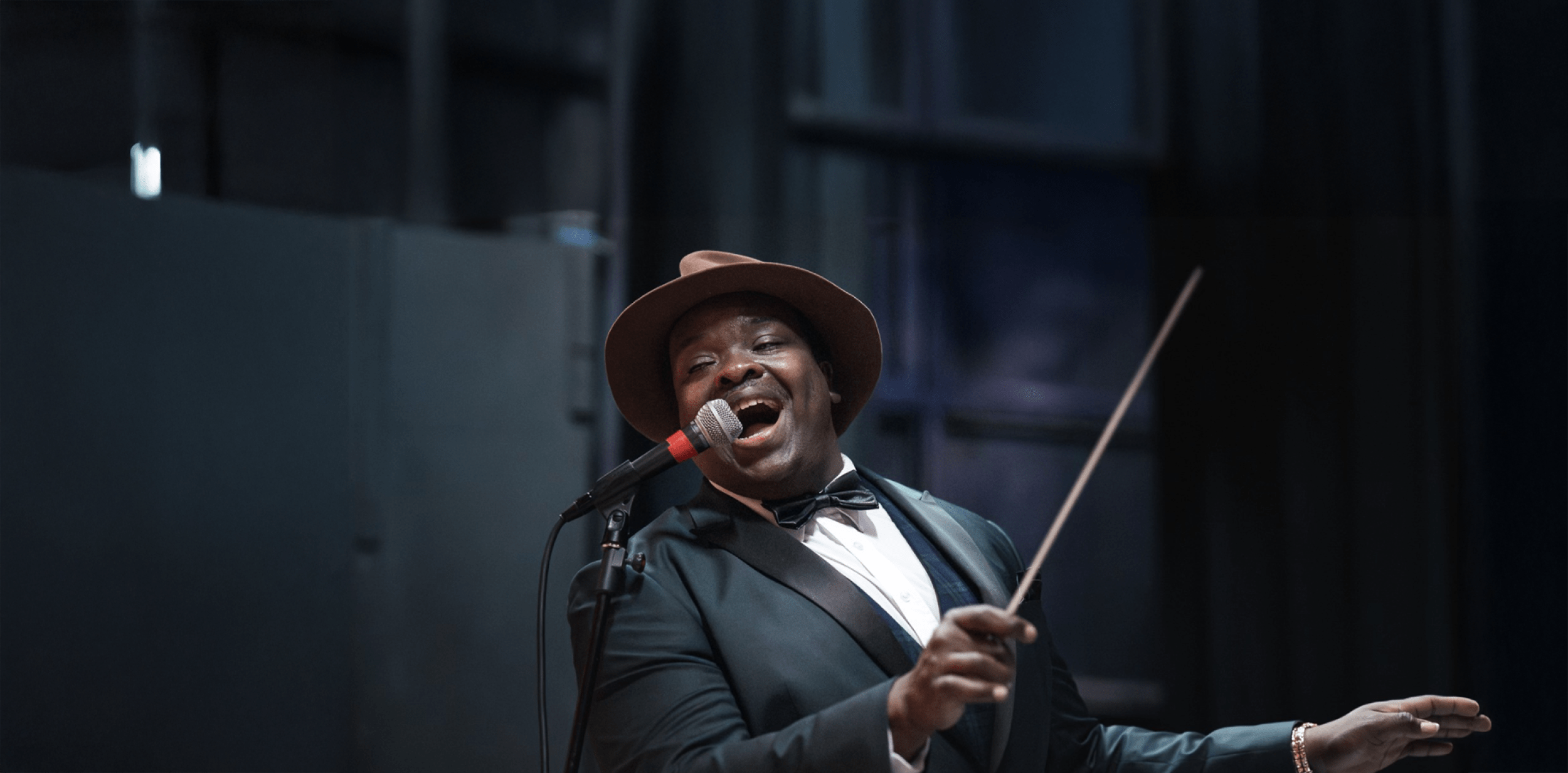 Marvin dressed in a suit and bow tie, singing into a mic and conducting.