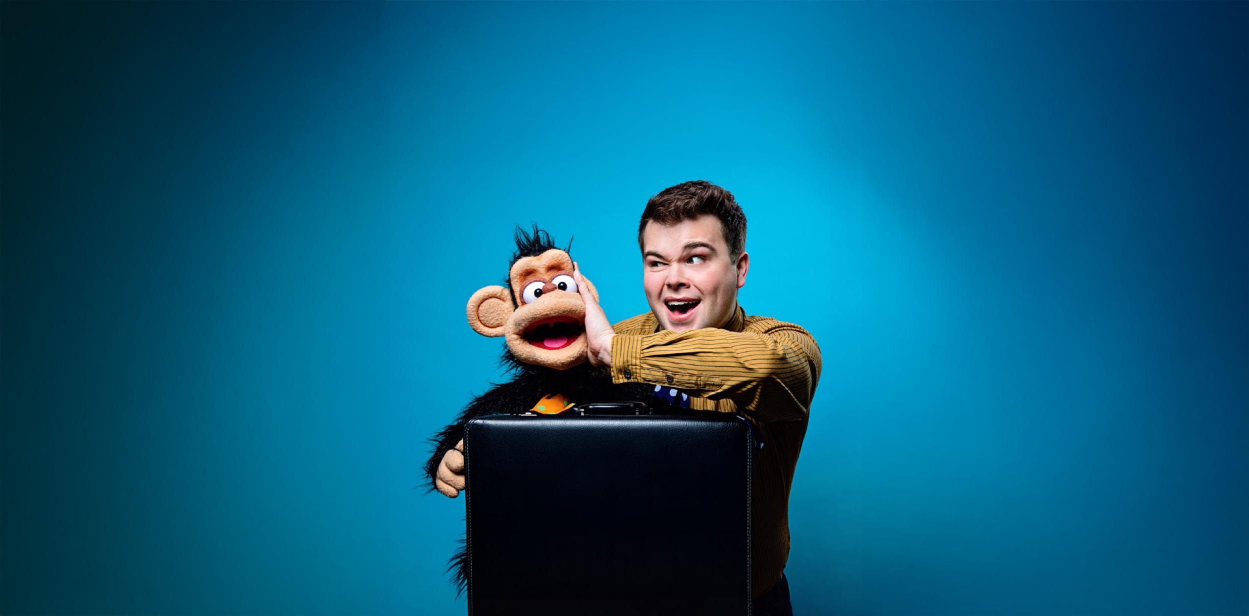 Max with a puppet monkey sitting on a suitcase with a blue background