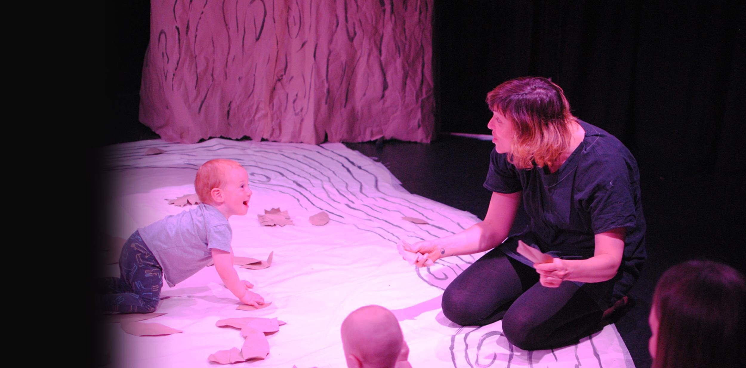 Baby smiling and crawling on mat looking at a female dressed in black