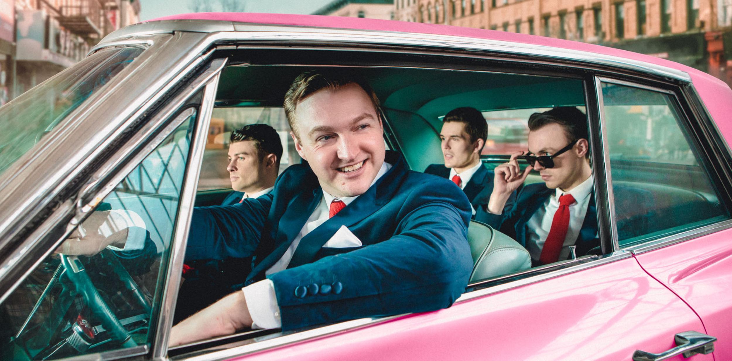 4 men in retro suits in a pink cadillac