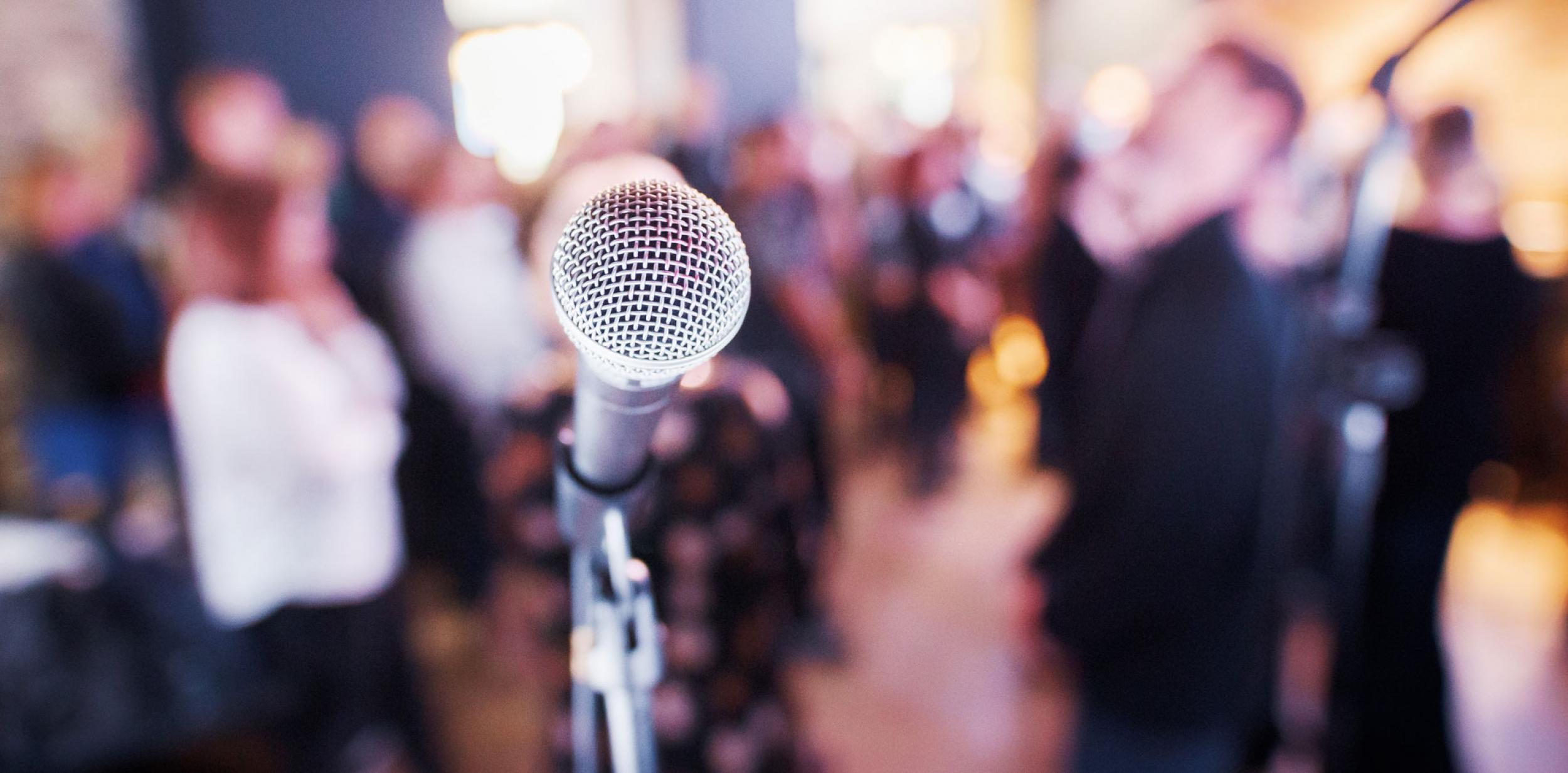 A microphone on a stand with a crowd of people behind it.