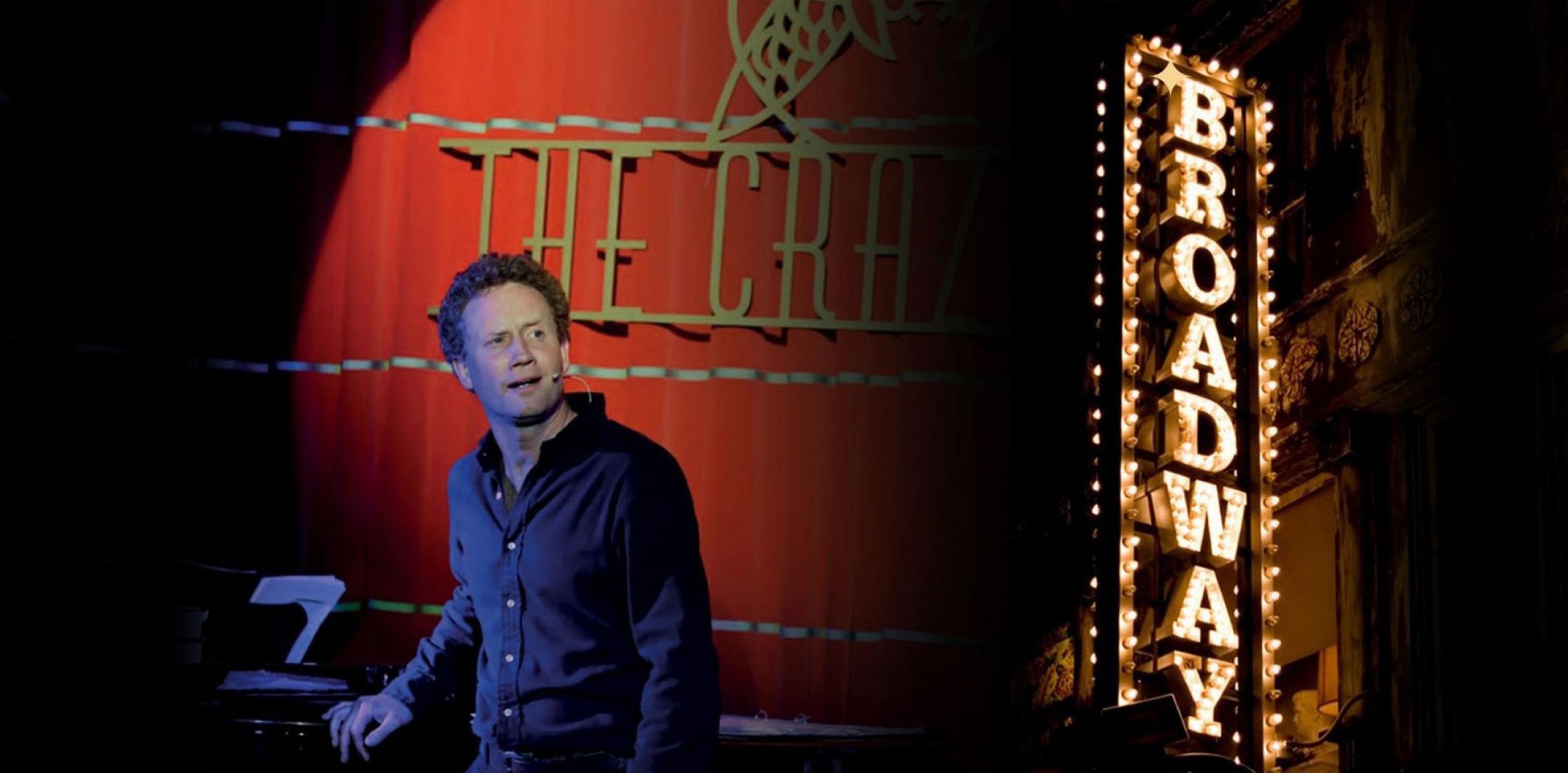 A person standing in front of a stage curtain with a Broadway sign in the background