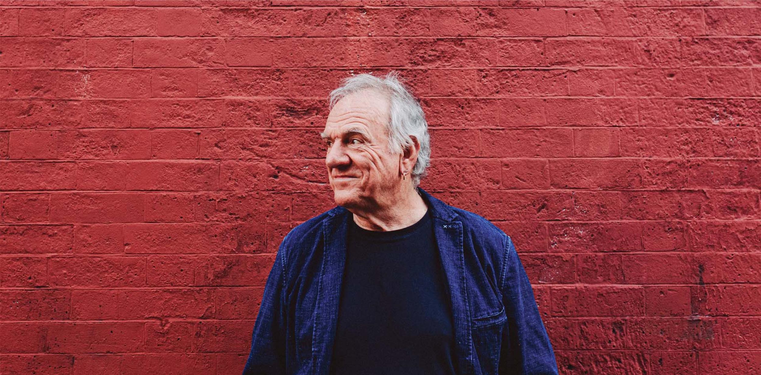 Ralph McTell looking to the left in front of a brick wall