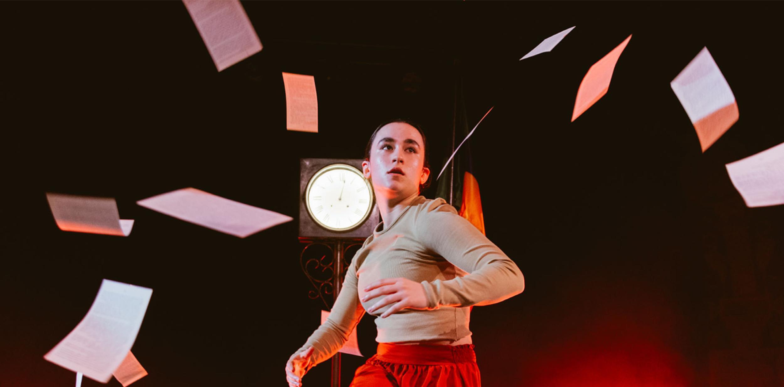 A performer dancing with sheets of paper flying around them.