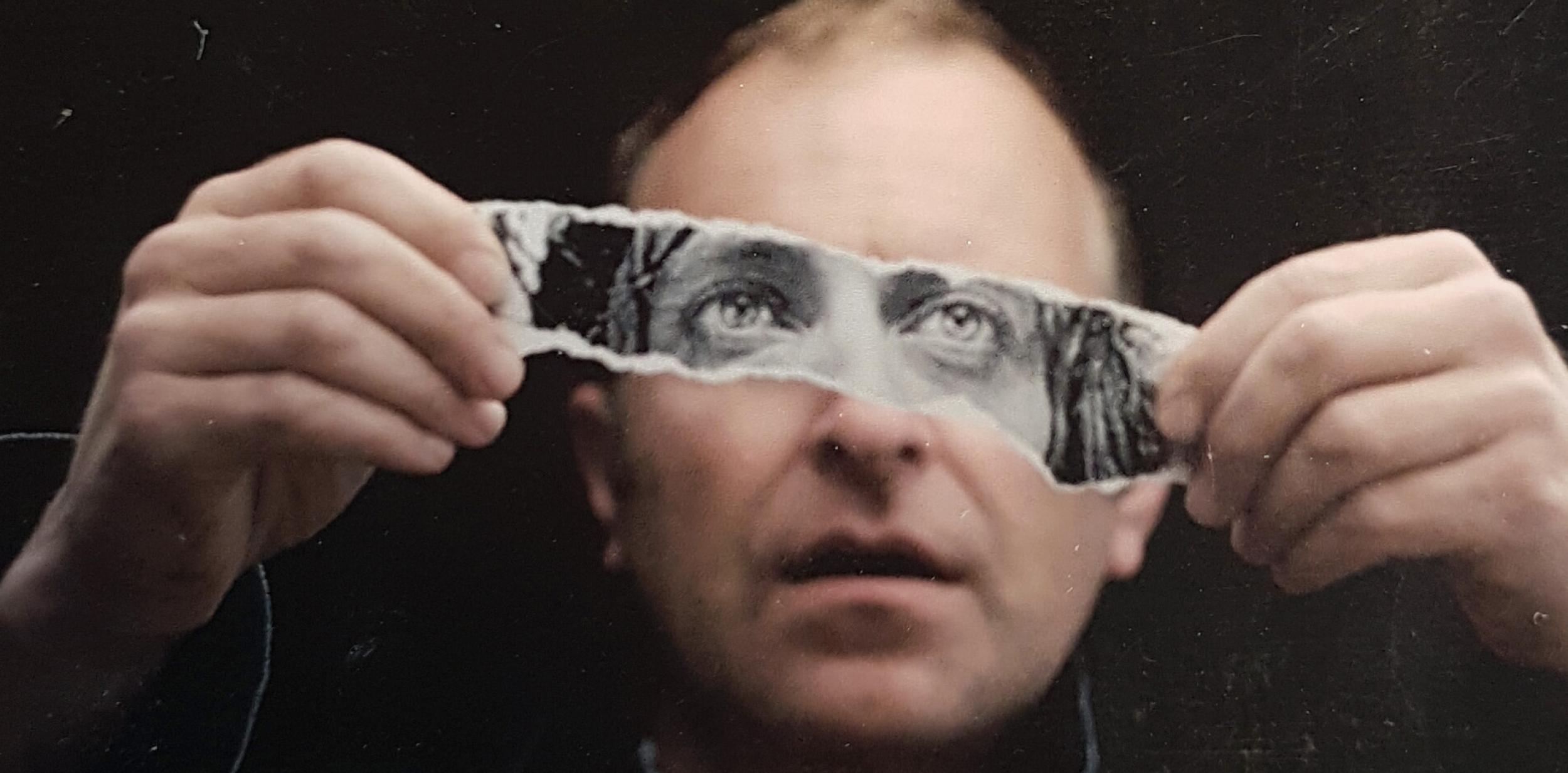 Man holding a strip of a photo over his eyes