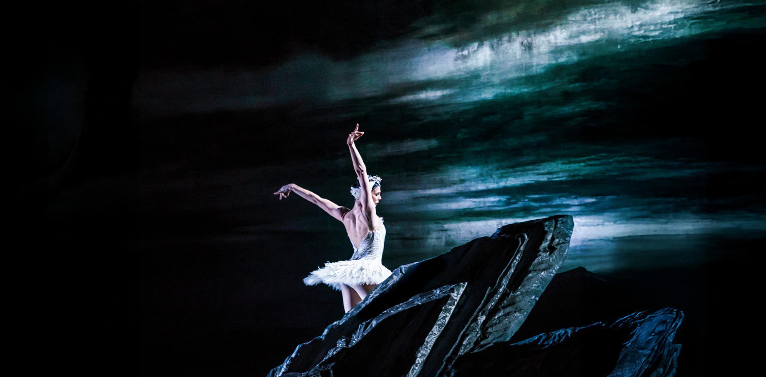 A ballet dancer dressed in white dancing on a dark structure.