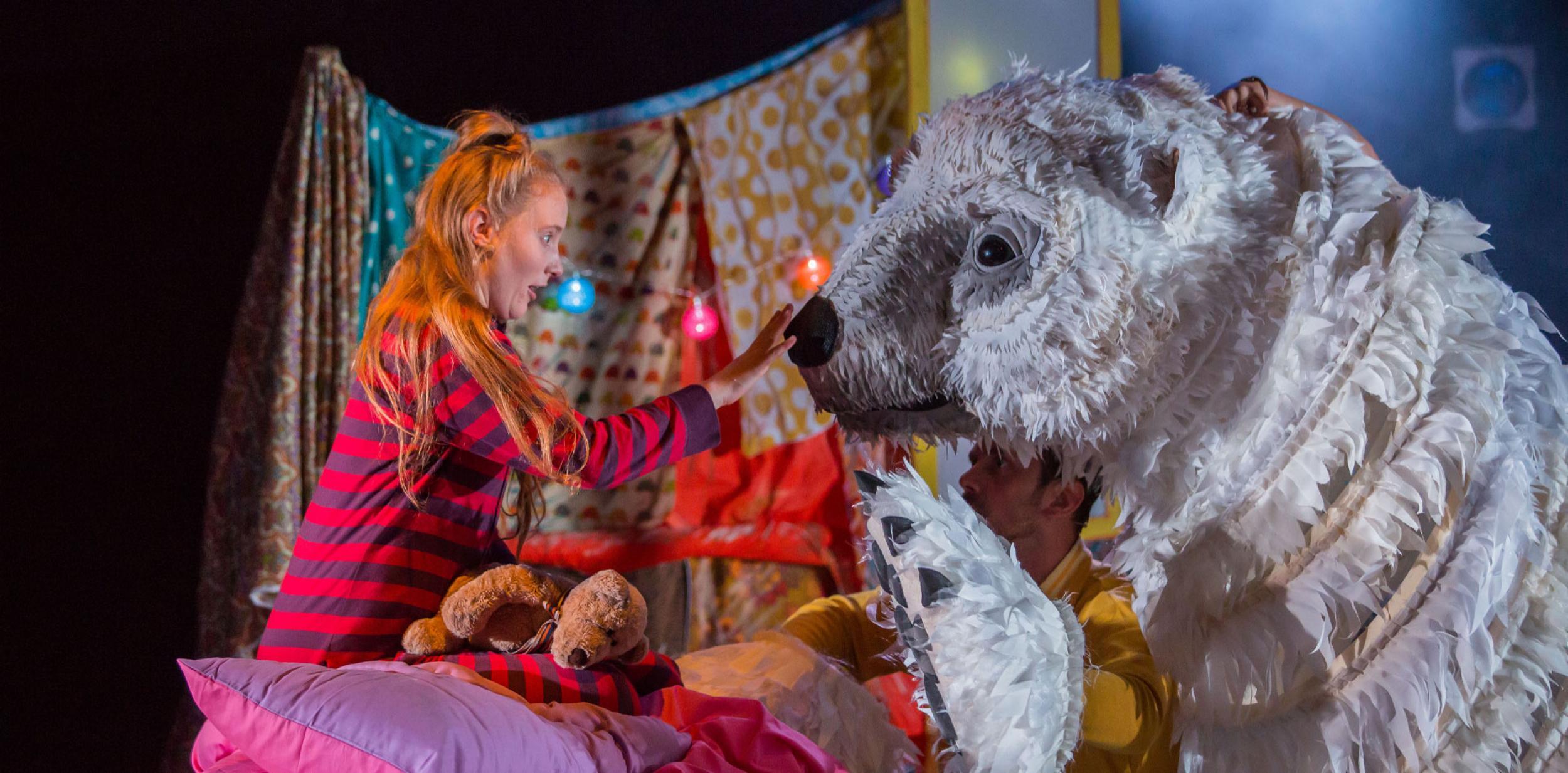 Girl reaching out towards the nose of a huge polar bear puppet.