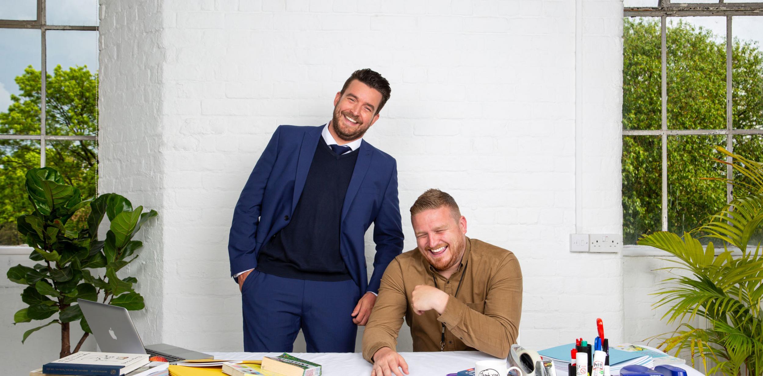Two men at a desk, laughing.
