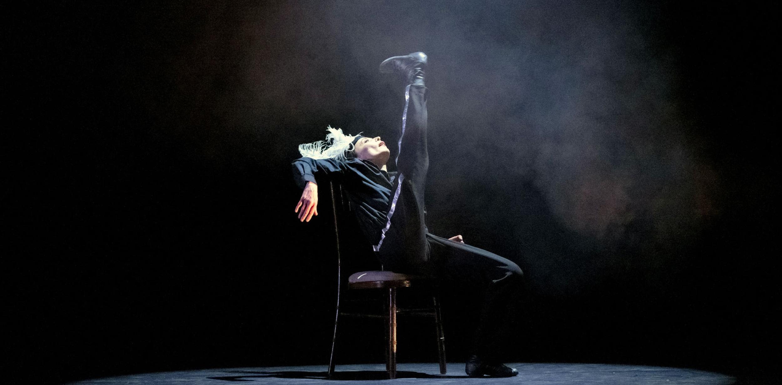 A dancer sitting in a chair and doing a high kick