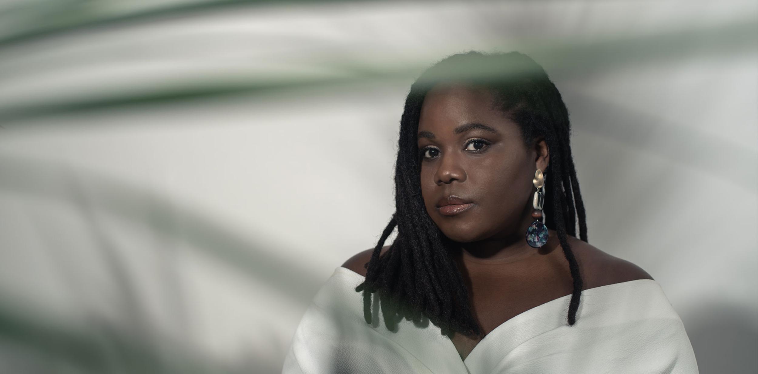 Zara McFarlane in white dress looking towards to the camera against a white shadowy background