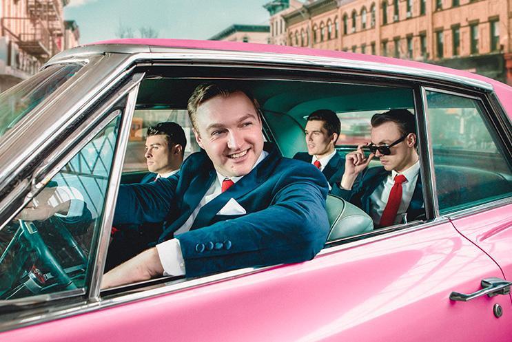4 men in retro suits in a pink cadillac