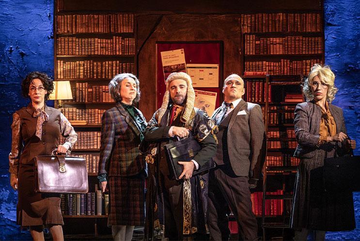 A group of people in period costume standing infront of a large bookcase