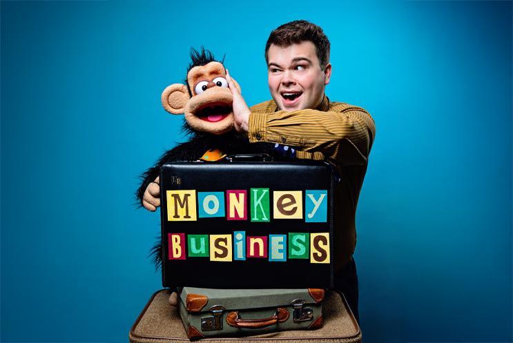 Max with a puppet monkey sitting on a suitcase with a blue background