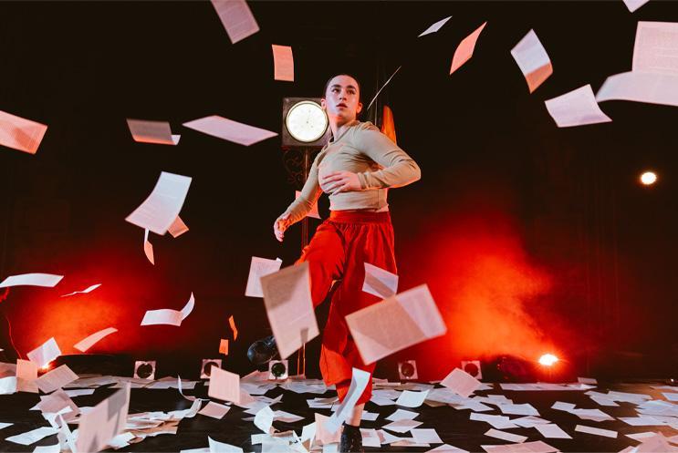 A performer dancing with sheets of paper flying around them.