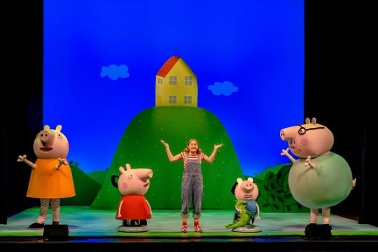 Peppa Pig & family on stage with a actress in front of a green hill