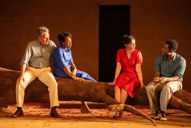 Four people sat on a fallen tree looking happy.