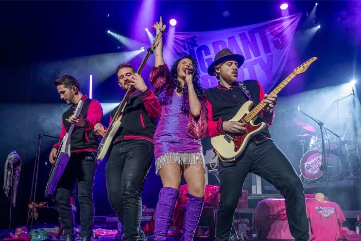 A woman singing into a mic with three musicians surrounding her.