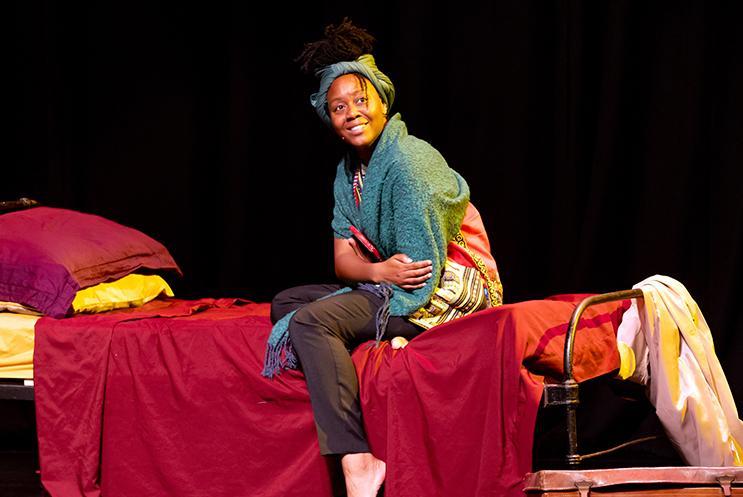 Performer sitting on a bed and smiling