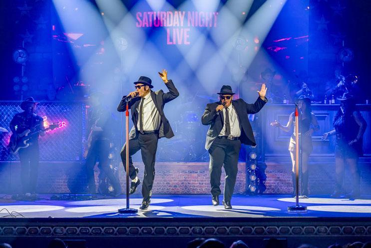 Two men in suits dancing and singing on stage.