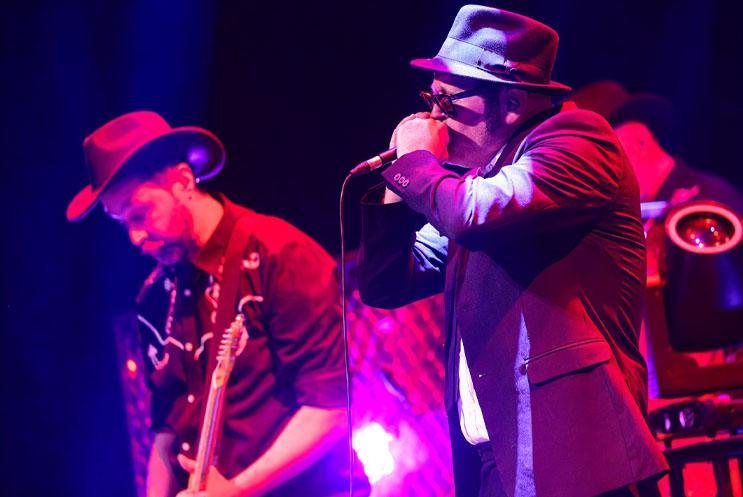 A man singing closely into a mic, anther man playing an instrument.