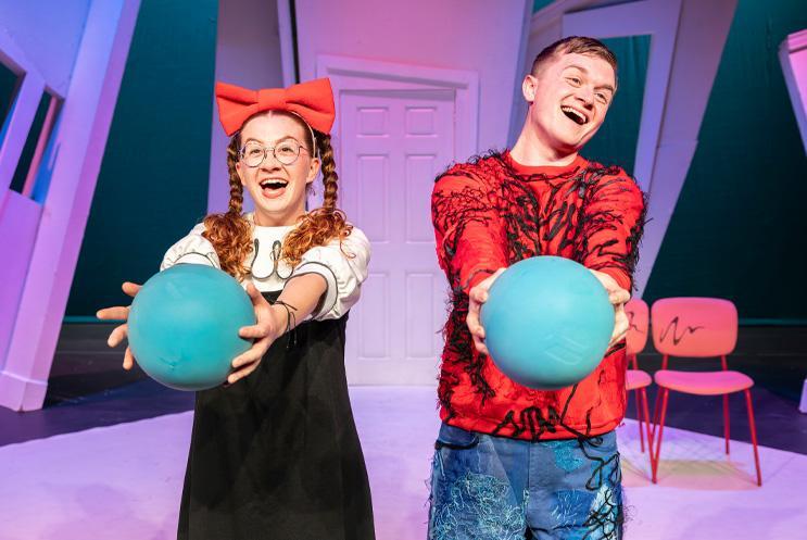 Two performers looking happy and holding blue balls.
