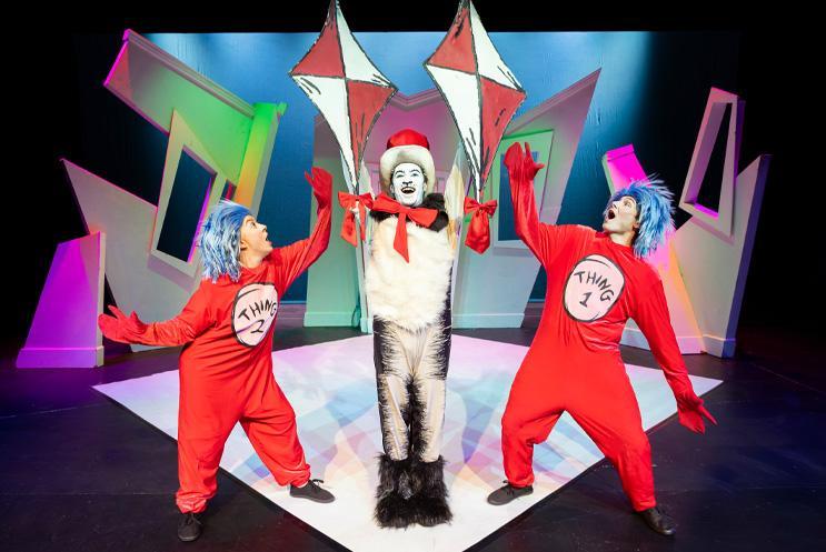 Cat holding up flags with two performers either side dressed in red costumes.