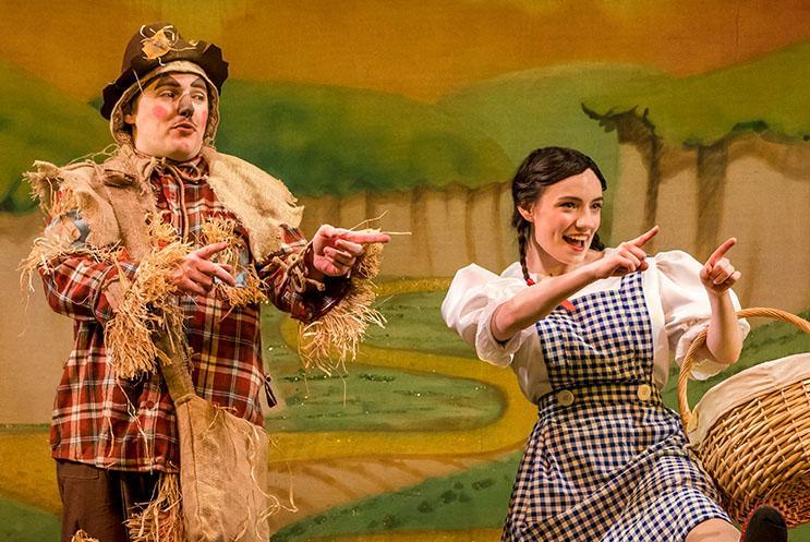 A scarecrow and a young girl dressed as Dorothy doing a dance