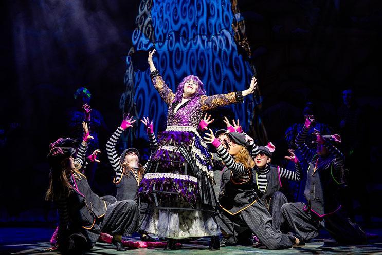 Panto villain doing a victory pose surround by an ensemble dressed as rats.