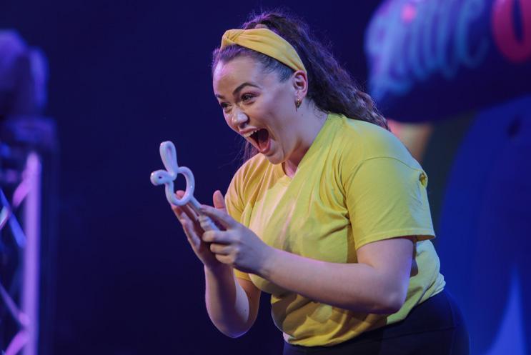 A woman in a yellow top looking excited at something she's holidng.