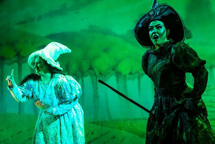 Glinda in a white dress and the Wikced Witch in a black dress shouting at the audience