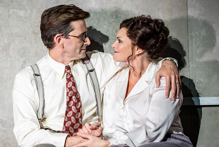 David Tennant and Sharon Small looking lovingly at each other. They are both sat together, their arms and hands intertwined.