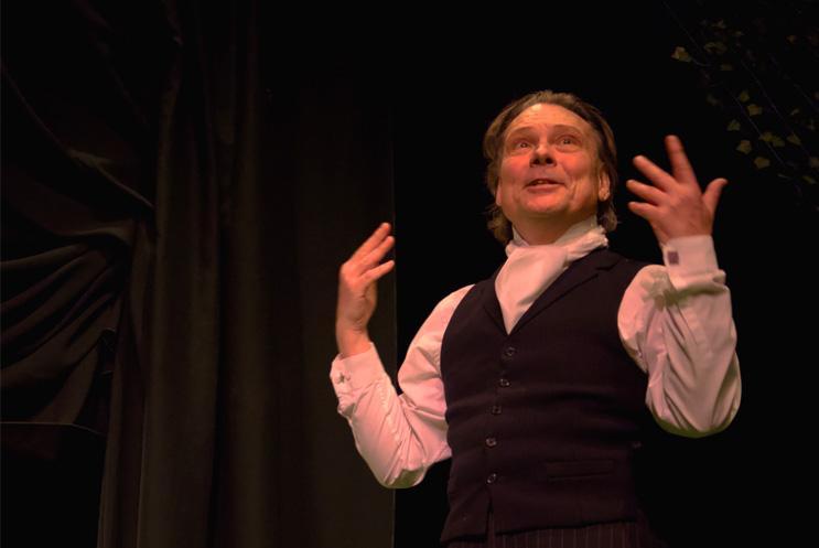 A man gesturing with his hands in front of a dark background.