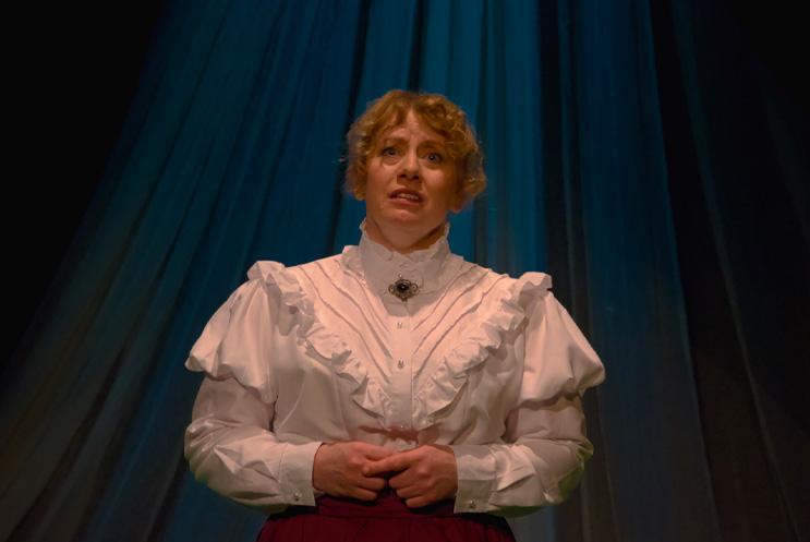 A woman in a white dress looking worried and clasping her hands together.