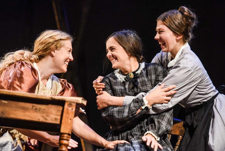 Three women in period drama costume, smiling and laughing.