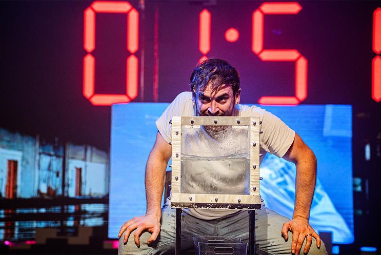 A performer putting his head into a glass box of water.